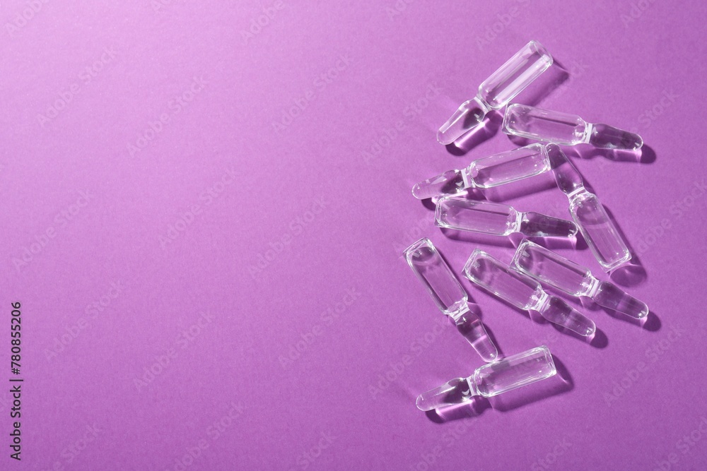 Glass ampoules with liquid on purple background, top view. Space for text Glass ampoules with liquid on purple background, top view. Space for text