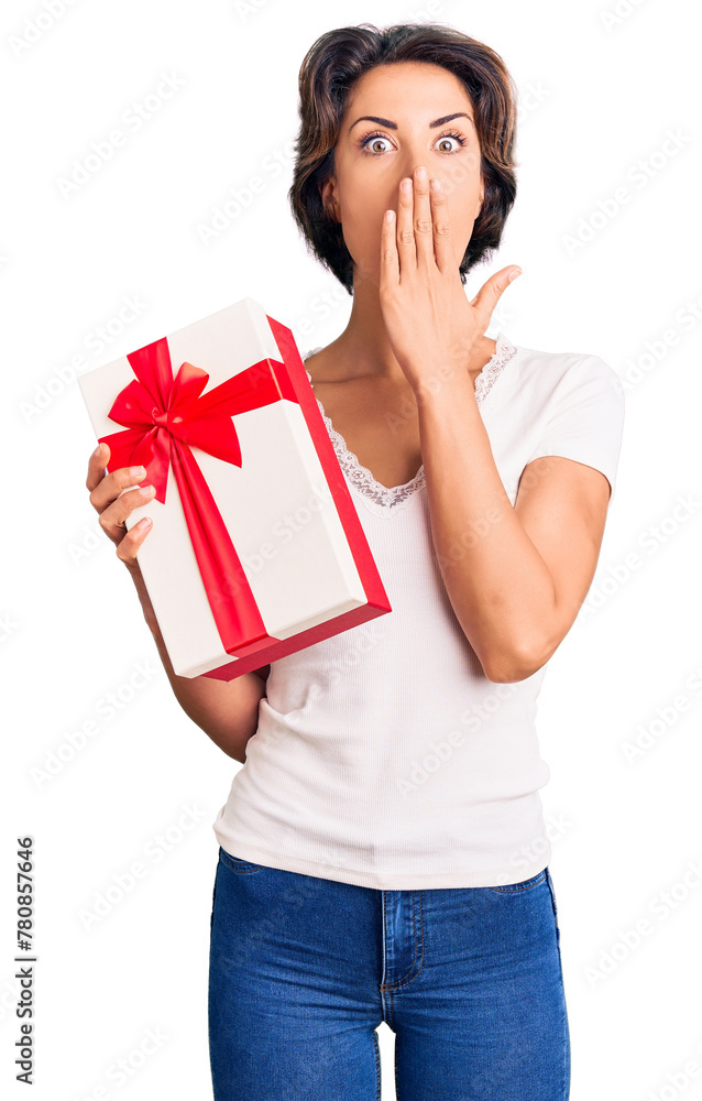Fototapeta premium Young beautiful woman holding gift covering mouth with hand, shocked and afraid for mistake. surprised expression