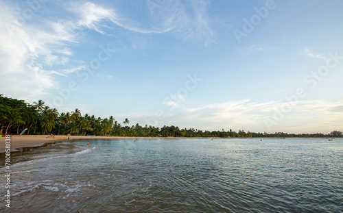 Praia do nordeste brasileiro com banhistas e luz suave de entardecer. Vegetação e coqueiros típicos do Brasil