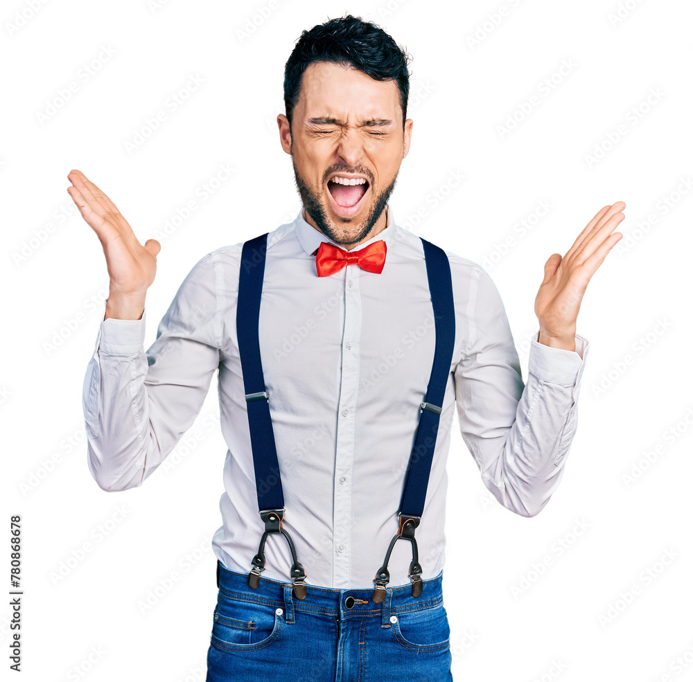 Φωτογραφία Hispanic man with beard wearing hipster look with bow tie and suspenders celebrating mad and crazy for success with arms raised and closed eyes screaming excited