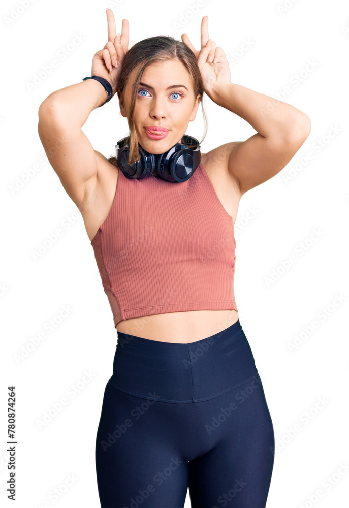 Beautiful caucasian young woman wearing gym clothes and using headphones doing bunny ears gesture with hands palms looking cynical and skeptical. easter rabbit concept. Beautiful caucasian young woman wearing gym clothes and using headphones doing bunny ears gesture with hands palms looking cynical and skeptical. easter rabbit concept.