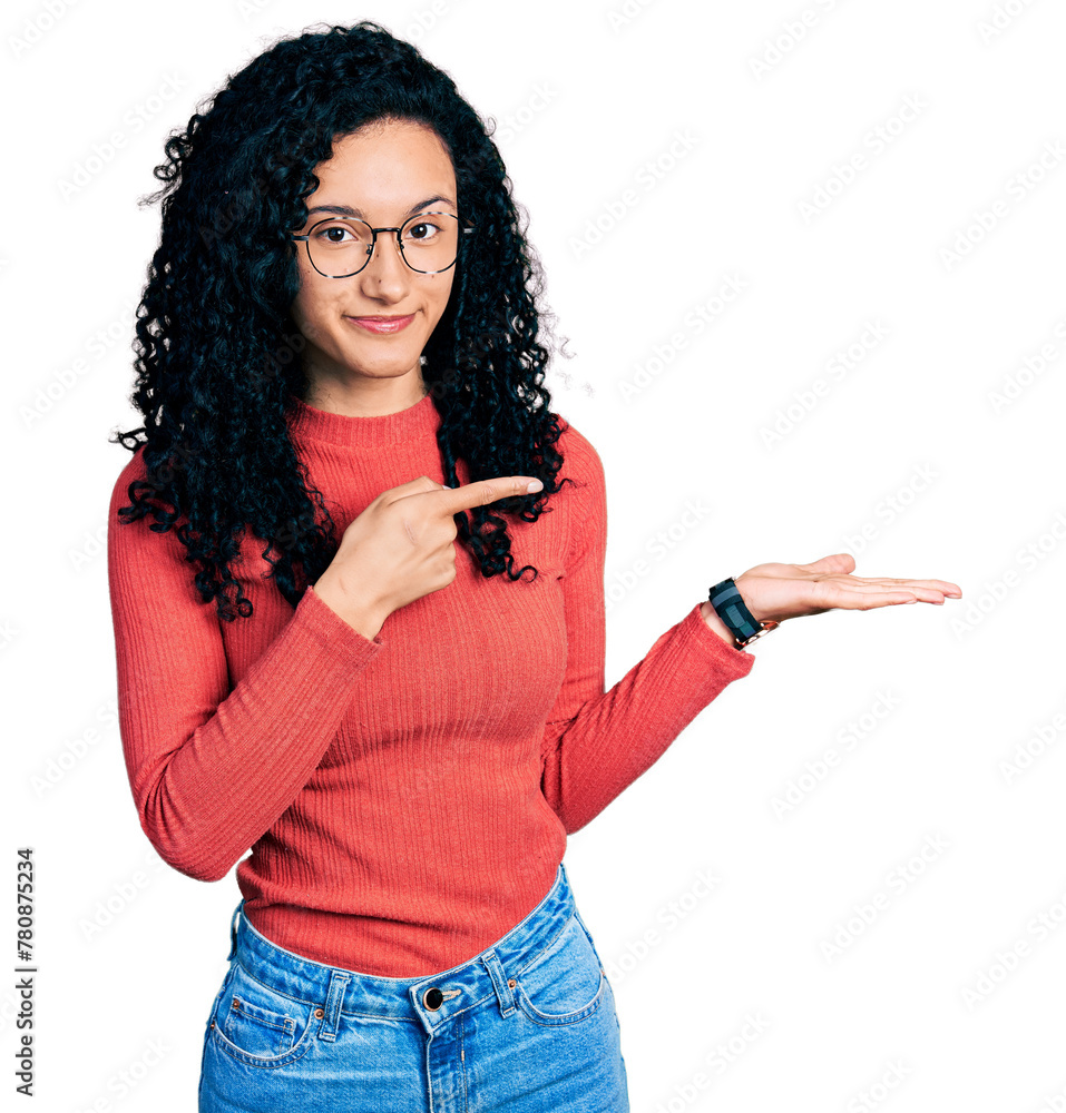 Young hispanic woman with curly hair wearing glasses amazed and smiling to the camera while presenting with hand and pointing with finger. Young hispanic woman with curly hair wearing glasses amazed and smiling to the camera while presenting with hand and pointing with finger.