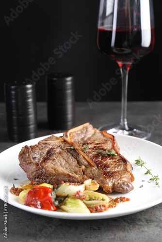 Delicious fried beef meat, vegetables and glass of wine on grey table