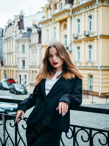 A woman in white shirt and a black jacket stands confidently on the street.