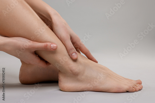 Woman suffering from leg pain on grey background, closeup © New Africa