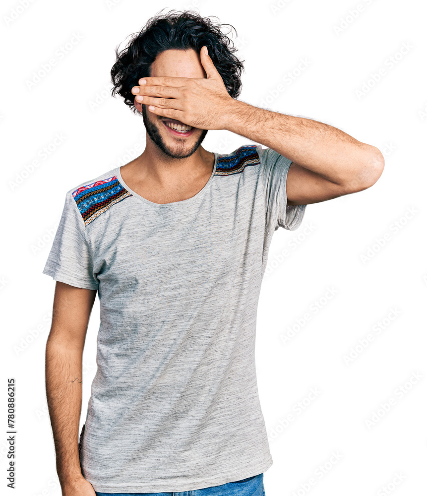 Young hispanic man wearing casual t shirt smiling and laughing with hand on face covering eyes for surprise. blind concept. Young hispanic man wearing casual t shirt smiling and laughing with hand on face covering eyes for surprise. blind concept.