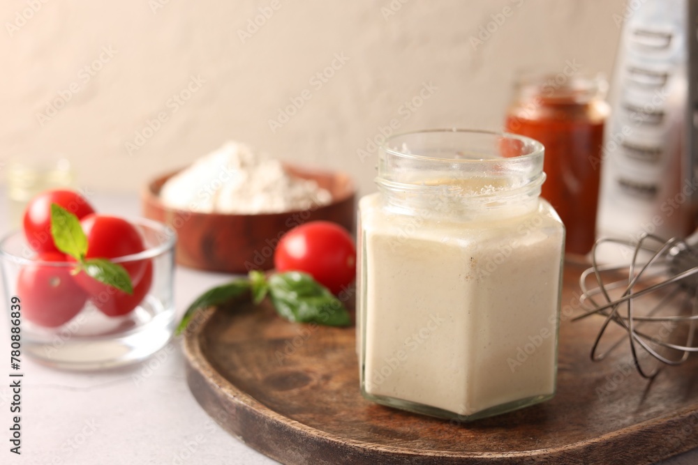 Pizza dough starter in glass jar, products and whisk on gray table Pizza dough starter in glass jar, products and whisk on gray table
