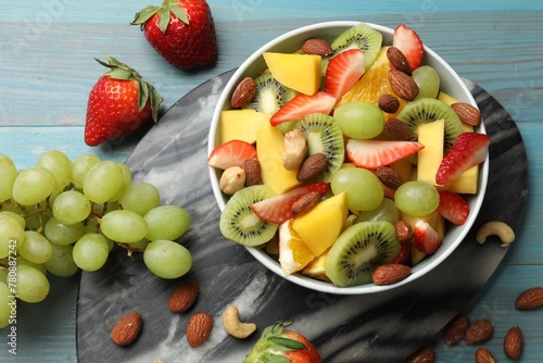 Tasty fruit salad in bowl and ingredients on light blue wooden table  flat lay