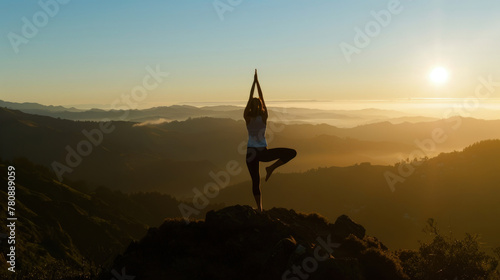 A person is performing a yoga pose on a mountain summit. The figure is balanced and focused, showcasing strength and flexibility amidst a scenic backdrop