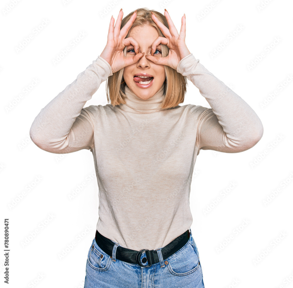 Young blonde woman wearing casual clothes doing ok gesture like binoculars sticking tongue out, eyes looking through fingers. crazy expression. Young blonde woman wearing casual clothes doing ok gesture like binoculars sticking tongue out, eyes looking through fingers. crazy expression.