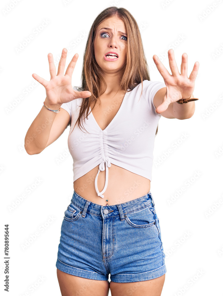 Young beautiful blonde woman wearing casual white tshirt afraid and terrified with fear expression stop gesture with hands, shouting in shock. panic concept.