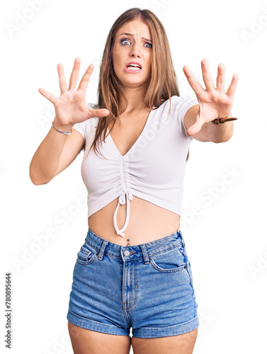 Young beautiful blonde woman wearing casual white tshirt afraid and terrified with fear expression stop gesture with hands, shouting in shock. panic concept.