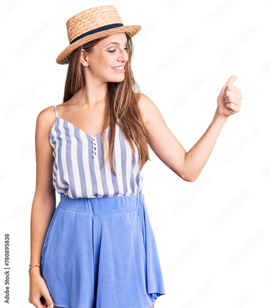Young beautiful blonde woman wearing summer hat looking proud, smiling doing thumbs up gesture to the side Young beautiful blonde woman wearing summer hat looking proud, smiling doing thumbs up gesture to the side