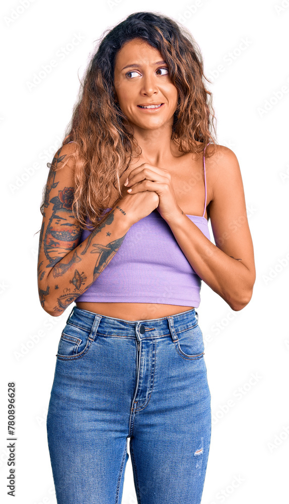 Young hispanic woman with tattoo wearing casual clothes laughing nervous and excited with hands on chin looking to the side Young hispanic woman with tattoo wearing casual clothes laughing nervous and excited with hands on chin looking to the side