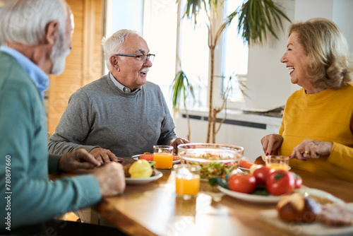 Group of happy mature friends talking while having a meal at dining table. 