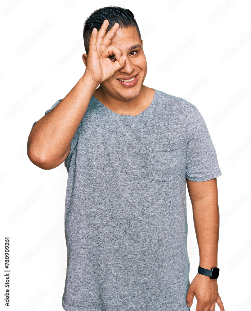 Young latin man wearing casual clothes doing ok gesture with hand smiling, eye looking through fingers with happy face. Young latin man wearing casual clothes doing ok gesture with hand smiling, eye looking through fingers with happy face.