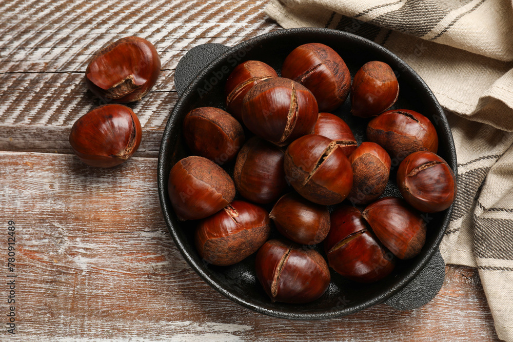 Fresh edible sweet chestnuts in frying pan on wooden table, flat lay Fresh edible sweet chestnuts in frying pan on wooden table, flat lay