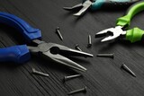 Different pliers and nails on black wooden table, closeup