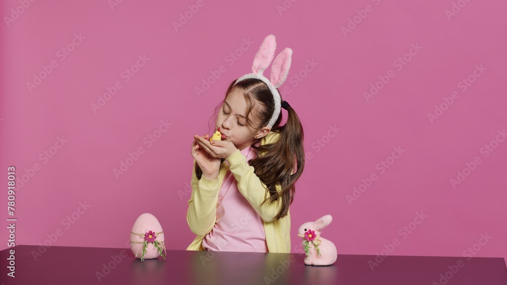 Obraz premium Joyful little girl playing with festive easter decorations in studio, creating arrangements with a chick, rabbit and egg. Smiling cute toddler with bunny ears showing colorful ornaments. Camera A.