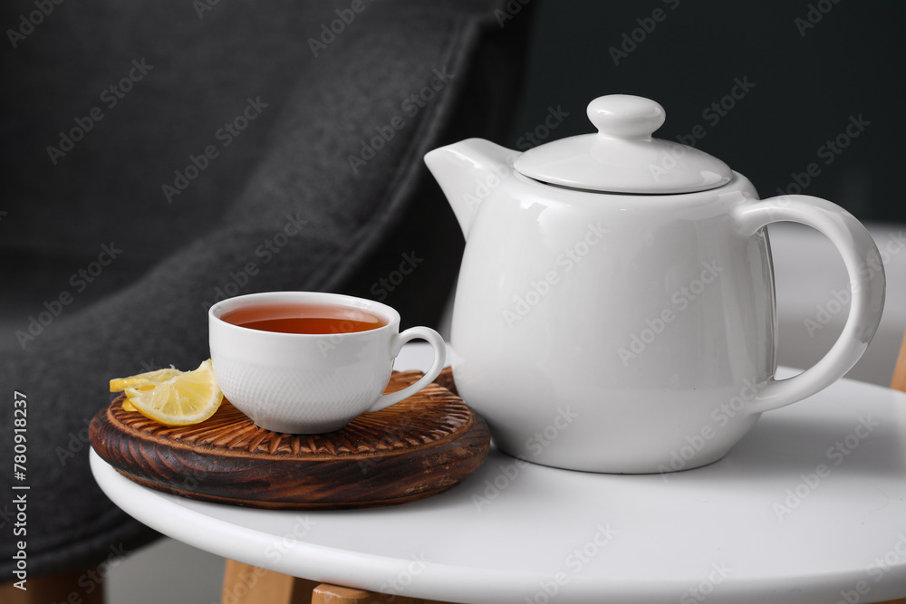 Board with cup of hot brewed tea, slices of lemon and pot on table against black blurred background Board with cup of hot brewed tea, slices of lemon and pot on table against black blurred background