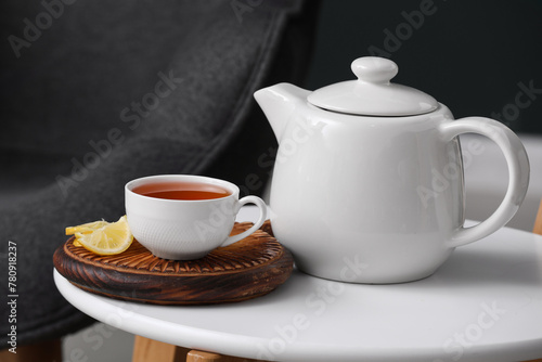 Board with cup of hot brewed tea, slices of lemon and pot on table against black blurred background