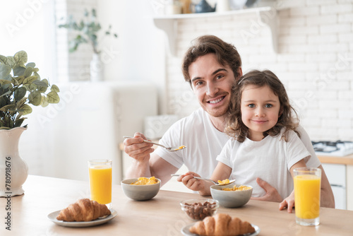 Young caring caucasian father feeding his small daughter with corn flakes in the morning for breakfast, family time, parenthood and fatherhood. Happy father`s day! I love you, dad!