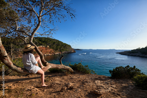 Woman sat on a tree looking at the see on a sunny day