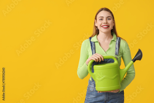 Happy young woman with watering can on yellow background