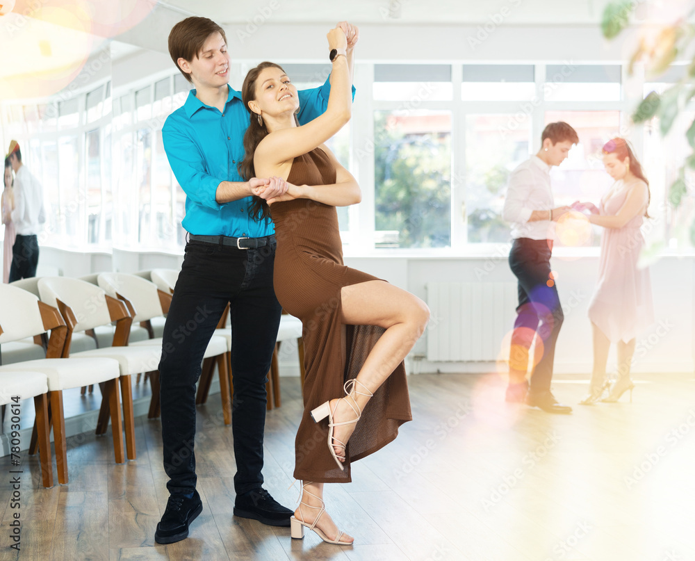Fototapeta premium Enthusiastic young couple, elegant guy and attractive girl in formal wear, performing kizomba in studio class setting, demonstrating dance characteristic sensual and connected movements..