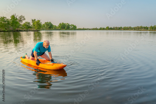 athletic, senior man is paddling a prone kayak on a lake in Colorado, this water sport combines aspects of kayaking and swimming