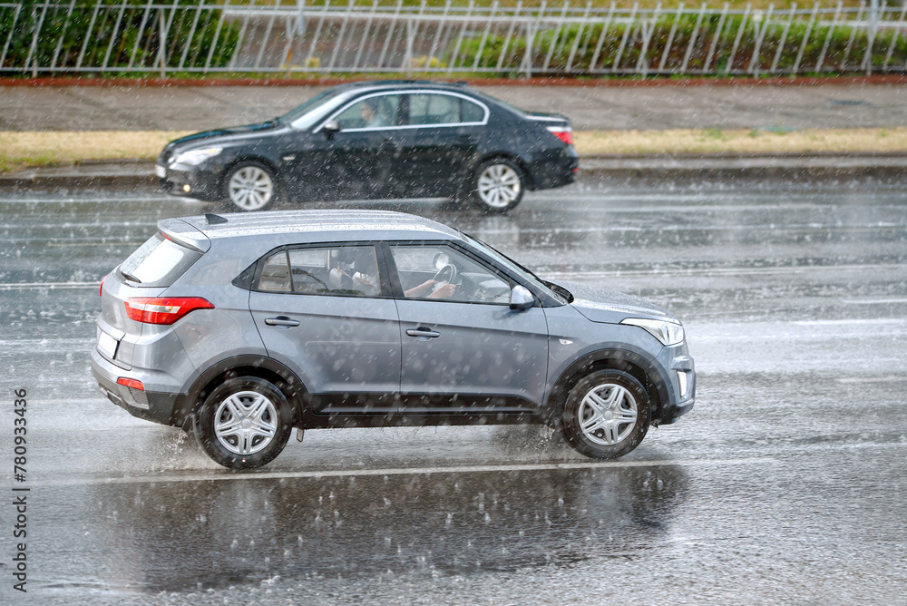 Cars driving fast through rain storm on city road, bad visibility. Car driving on flooded road, risks of driving in rainy weather. Car driving in wet weather conditions, avoid accidents.