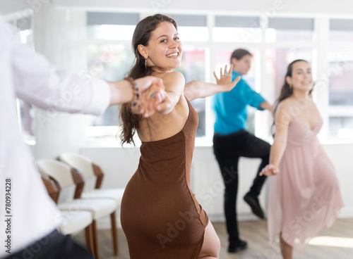 Cheerful enthusiastic young girl rehearsing upbeat jive dance moves with male partner in bright studio. Active hobby concept..