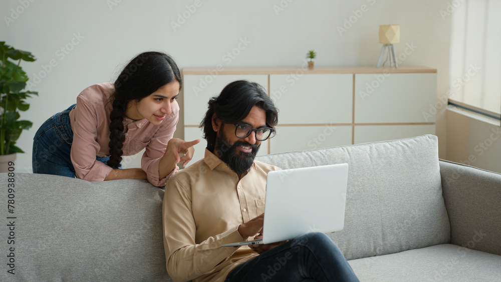 Arabian Indian couple on couch sofa use computer laptop shopping online internet store excited multiracial wife husband happy excited customers woman and man search goods purchase on website at home Arabian Indian couple on couch sofa use computer laptop shopping online internet store excited multiracial wife husband happy excited customers woman and man search goods purchase on website at home
