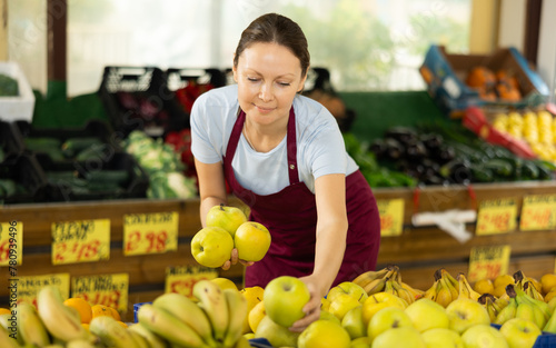 Woman seller working in supermarket and lays out fresh apples on counter