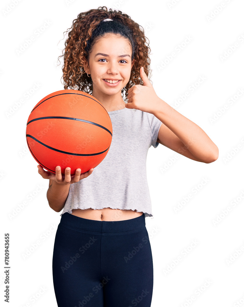 Beautiful kid girl with curly hair holding basketball ball smiling happy and positive, thumb up doing excellent and approval sign