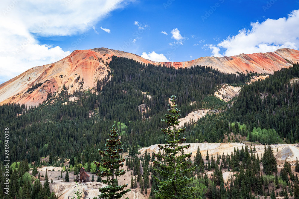 Red Mountain peaks and forest summer landscape of pine trees in the San Juan Mountains of southwest Colorado, USA with blue sky and white clouds.