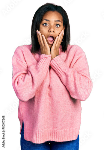 Beautiful hispanic woman wearing casual winter sweater afraid and shocked, surprise and amazed expression with hands on face