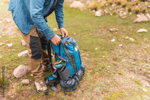 hands of mountaineer unpacking blue hiking backpack in the mountain surrounded by green vegetation and natural sunlight