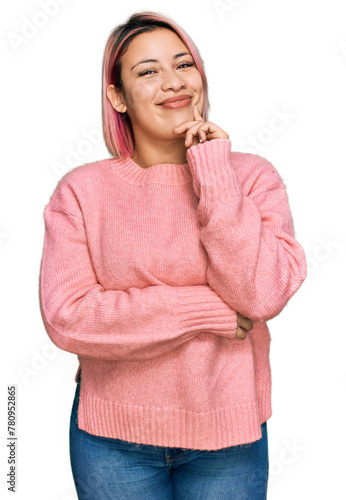 Hispanic woman with pink hair wearing casual winter sweater looking confident at the camera smiling with crossed arms and hand raised on chin. thinking positive.