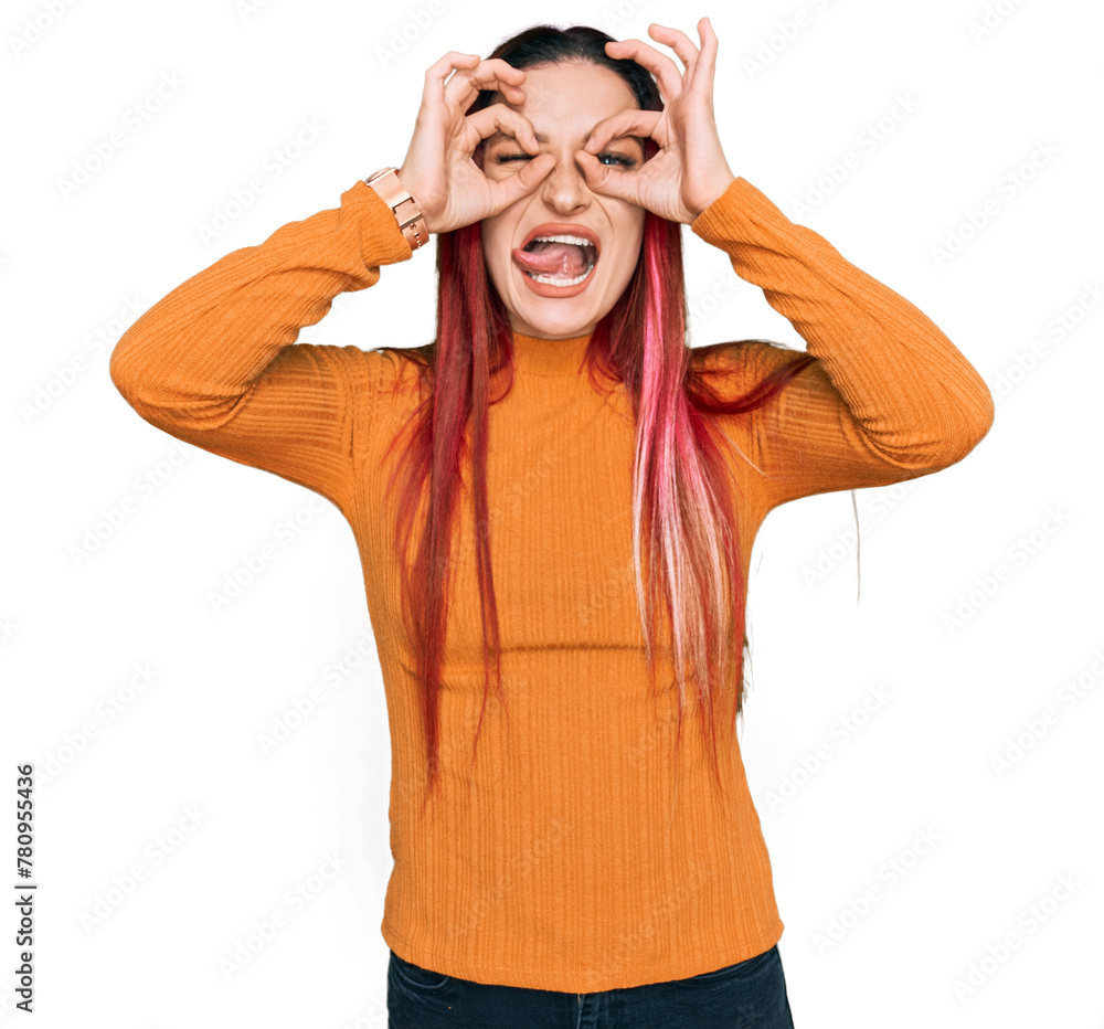 Naklejka premium Young caucasian woman wearing casual clothes doing ok gesture like binoculars sticking tongue out, eyes looking through fingers. crazy expression.