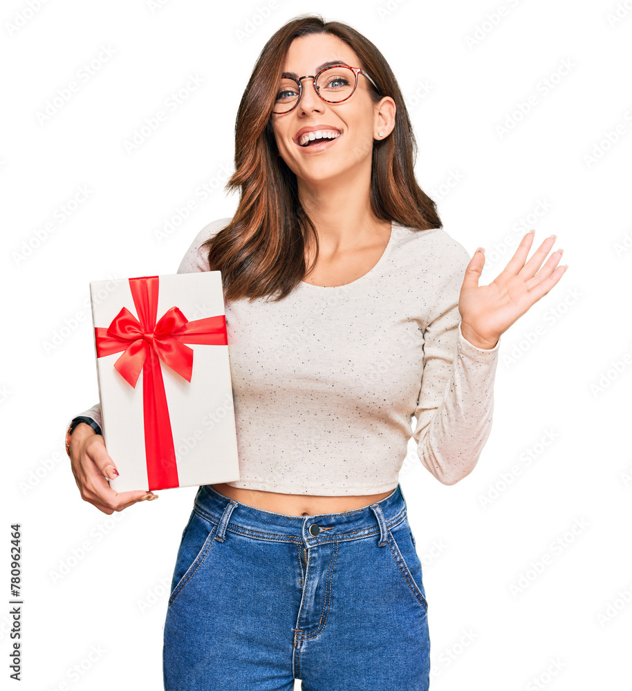 Young brunette woman holding gift celebrating victory with happy smile and winner expression with raised hands Young brunette woman holding gift celebrating victory with happy smile and winner expression with raised hands