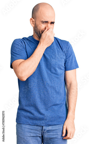 Young handsome man wearing casual t shirt smelling something stinky and disgusting, intolerable smell, holding breath with fingers on nose. bad smell