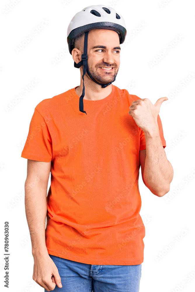 Young handsome man wearing bike helmet smiling with happy face looking and pointing to the side with thumb up. Young handsome man wearing bike helmet smiling with happy face looking and pointing to the side with thumb up.