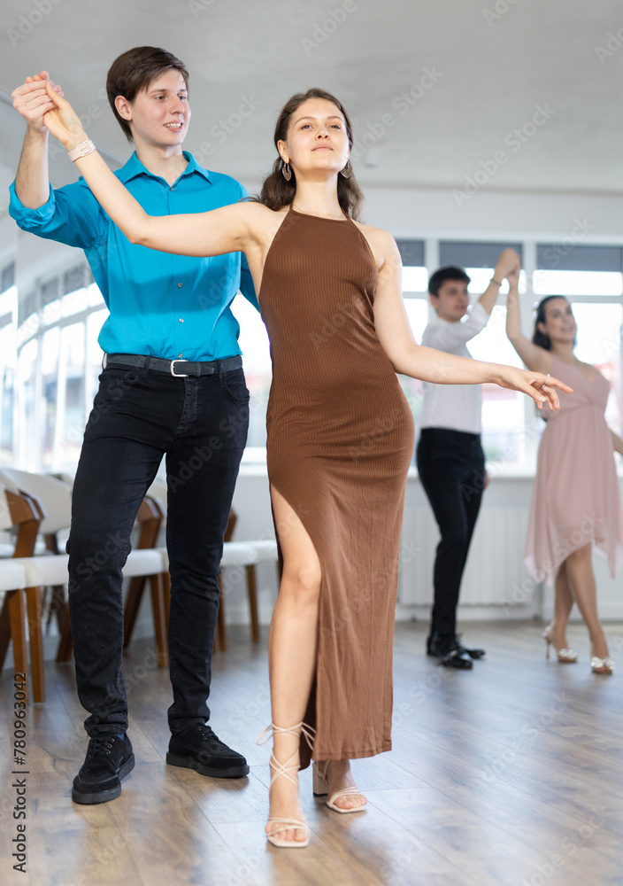 Fototapeta premium Enthusiastic young couple, elegant guy and attractive girl in formal wear, performing kizomba in studio class setting, demonstrating dance characteristic sensual and connected movements..