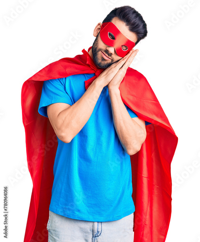 Young handsome man with beard wearing super hero costume sleeping tired dreaming and posing with hands together while smiling with closed eyes.