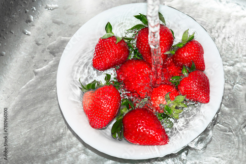 Plate of fresh delicious ripe strawberries washed under running water.