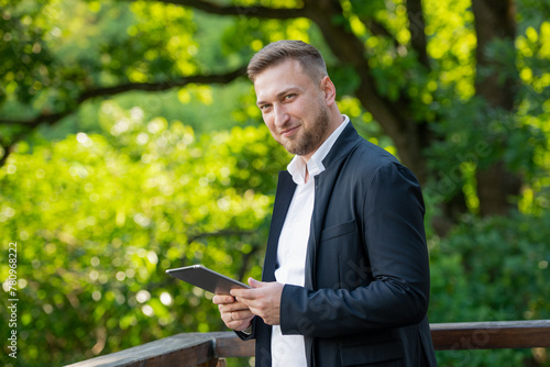 Φωτογραφία friendly businessman with a tablet against a background of green trees