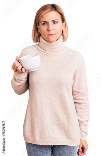 Young blonde woman holding coffee thinking attitude and sober expression looking self confident