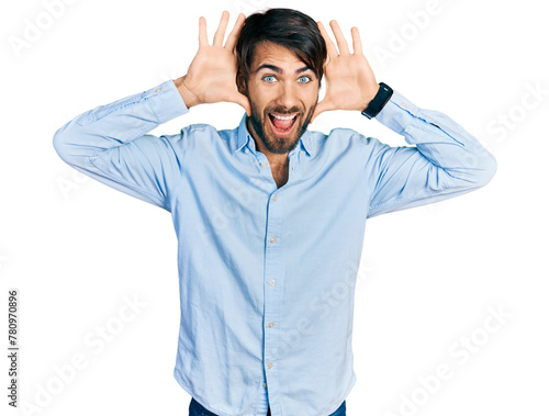 Hispanic man with blue eyes wearing business shirt smiling cheerful playing peek a boo with hands showing face. surprised and exited