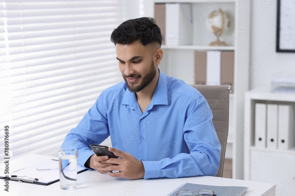 Handsome young man using smartphone at white table in office Handsome young man using smartphone at white table in office